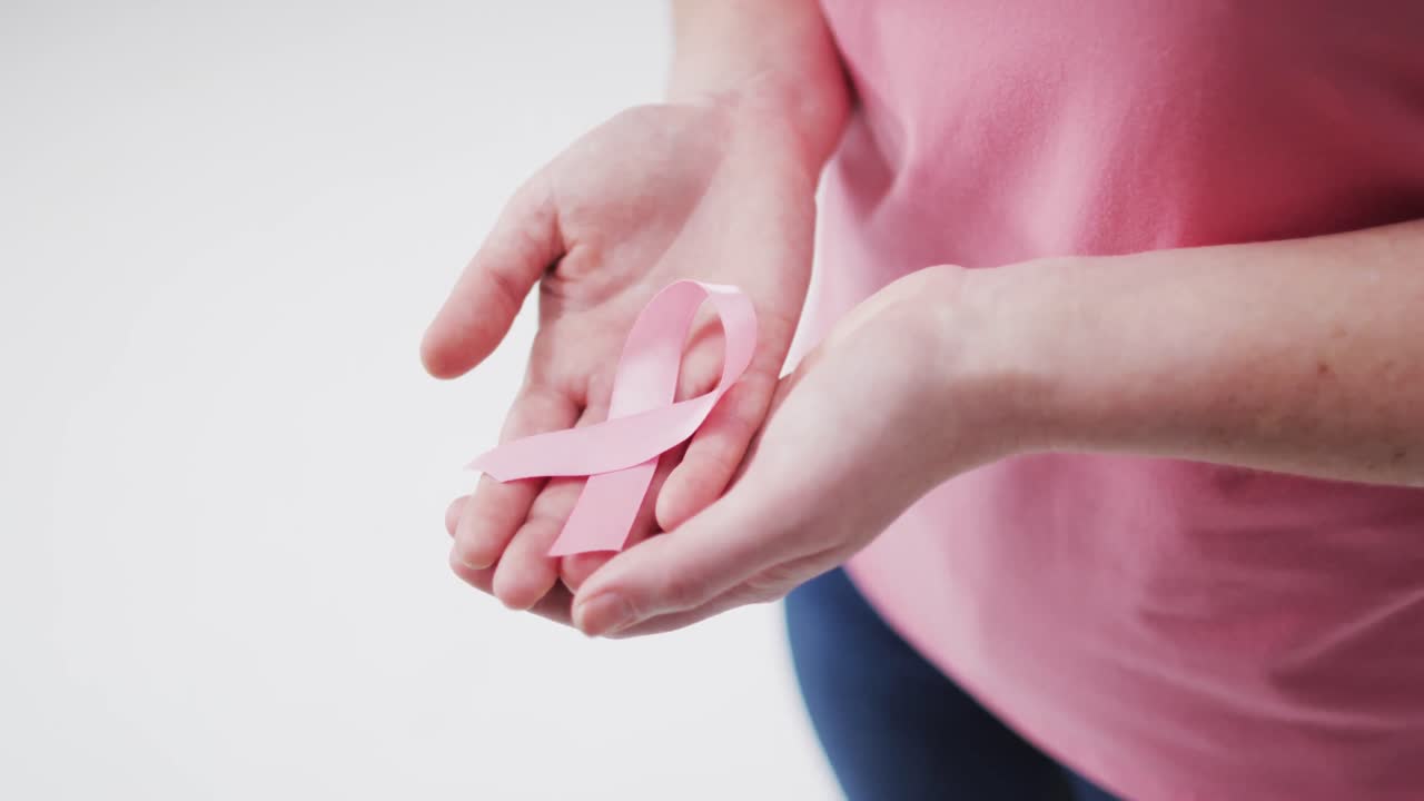 Mezzo busto di donna che tiene un nastro rosa su sfondo bianco.