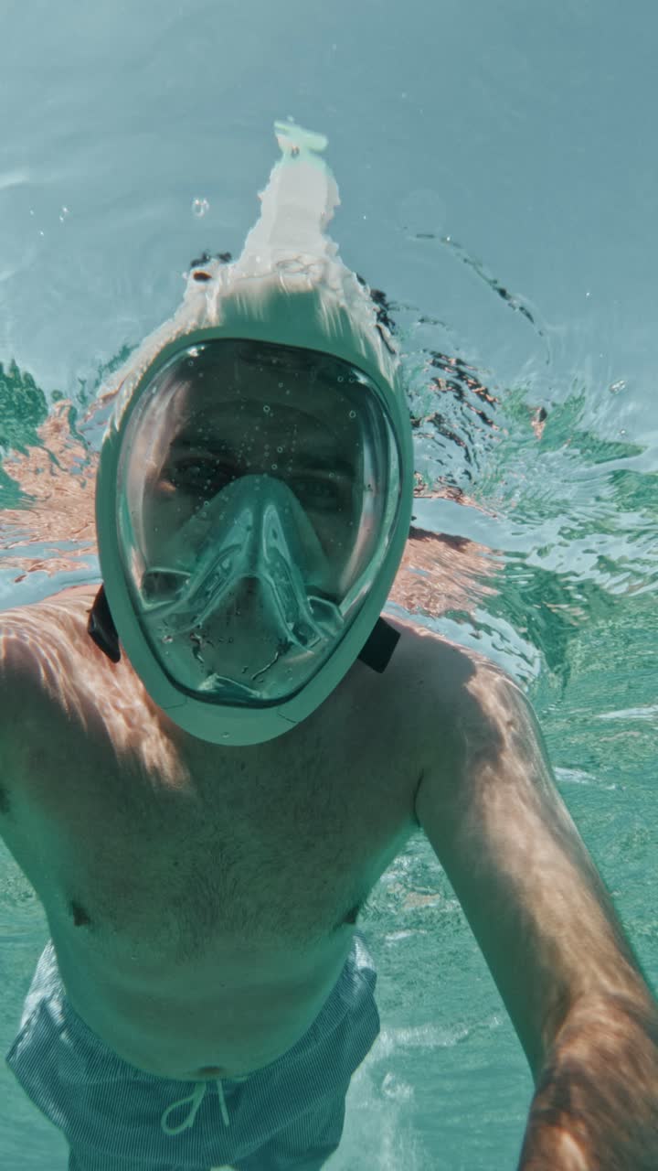 A Man With a Full-face Snorkel Mask Glides Beneath the Surface in Crystal-clear Water - Vertical Shot