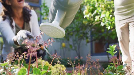 Mixed-race-mother-and-daughter-gardening-in-sunny-garden,-watering-plants