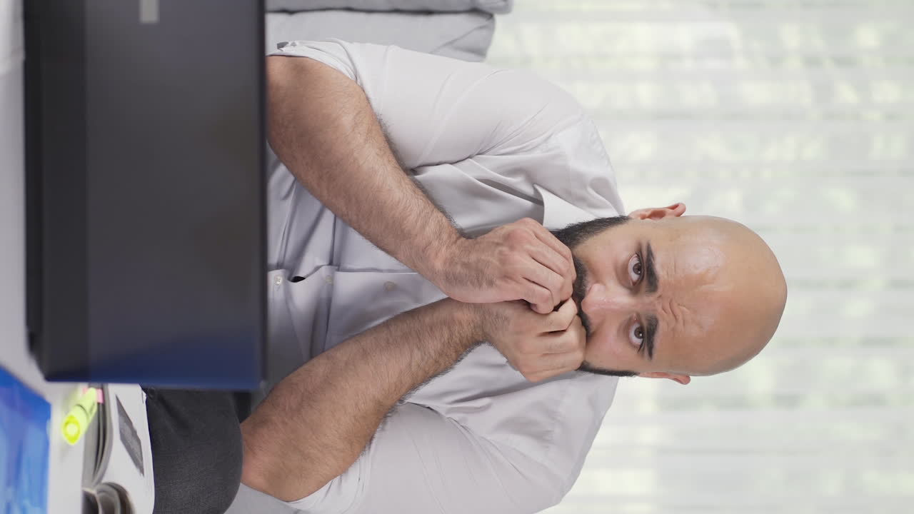 Vertical video of Home office worker man biting his nails looking at camera.