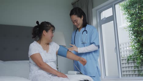 smiling asian female doctor taking blood pressure of happy female patient at hospital