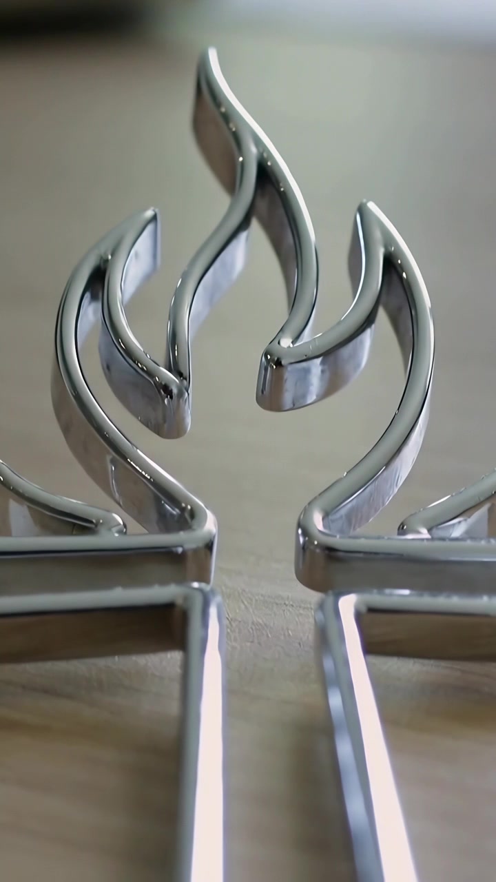 Video verticale: Telecamera che scorre rivelando un emblema cromato da centrare su un tavolo di legno chiaro, con un libro sfocato.