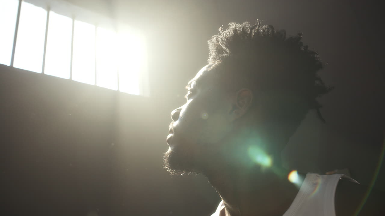 Pensive Inmate Gazing Upward with Arms behind Head in Sunlit Prison Cell