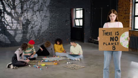 serious young environmental activist holding a cardboard with there is no planet b" inscription and looking at the camera"