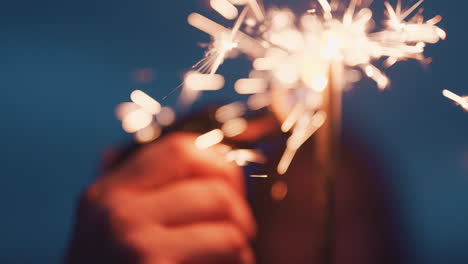 close up hand lighting sparkler celebrating new years eve on beach at night watching beautiful sparks