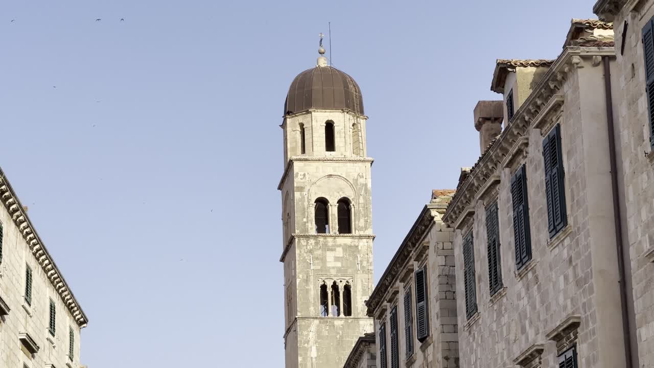 Clip cinematografica che svela i tetti di Stradun nella città vecchia di Dubrovnik, con le mura della città, la bandiera di Dubrovnik, il campanile della chiesa e gli uccelli che volano nella golden hour del primo mattino [travel b-roll]