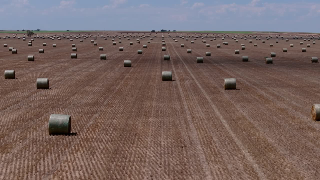 High drone descend tilt up revealing vast flat field and isolated hay bales across agriculture farmland, nobody