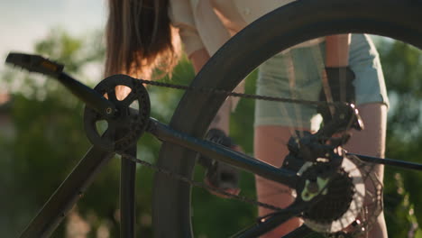 close-up of lady bending to turn bike pedal with her hand, causing back tire to rotate, highlighting motion and mechanics of cycling, background includes green foliage