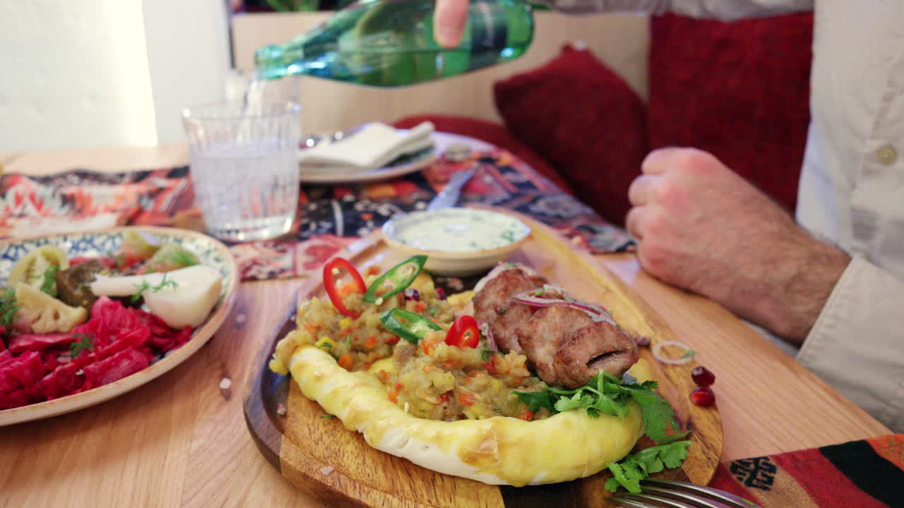 Primo piano di una donna che taglia carne alla griglia su pane piatto, servito con salsa cremosa e verdure.