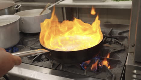 slow motion shot of onions being sautéed by a restaurant kitchen staff in hot oil creating an impressive flame