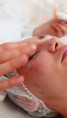 Adult woman receiving under eye cream application by beautician in cosmetology clinic for skincare