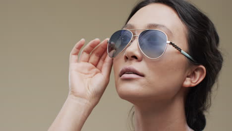mujer asiática con cabello oscuro y gafas de sol con espacio de copia en fondo beige, cámara lenta