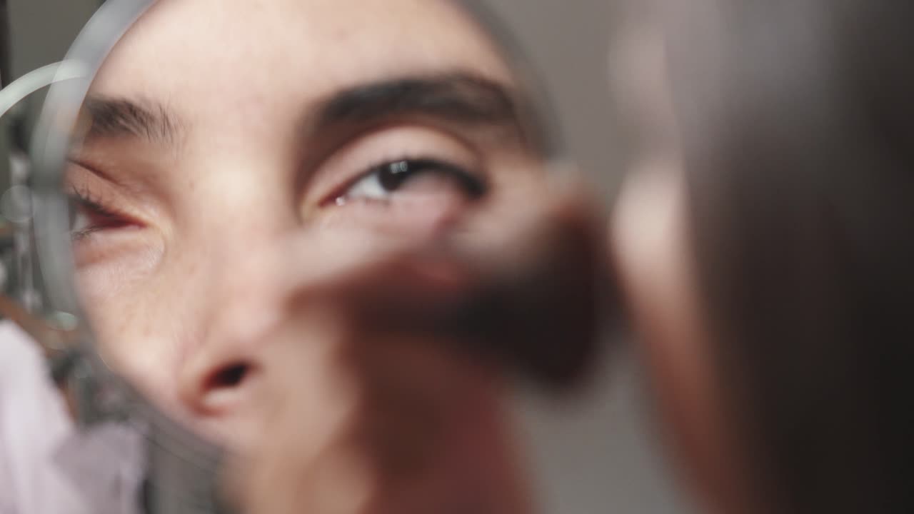 atractiva mujer joven que se maquilla con un cepillo que agrega bronceador en la cara