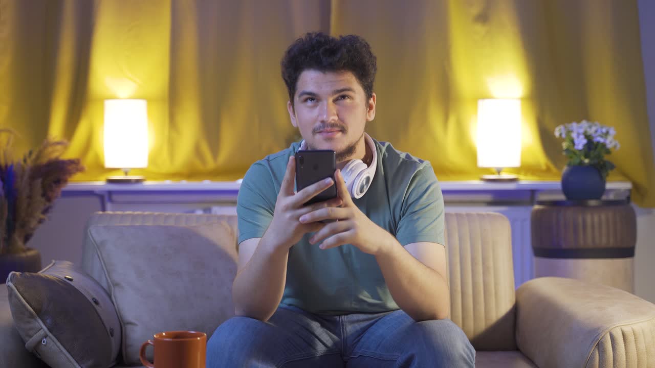 ⁇ 드폰으로 소셜미디어를 사용하는 남자가 밤에 집에서 웃고 있습니다.