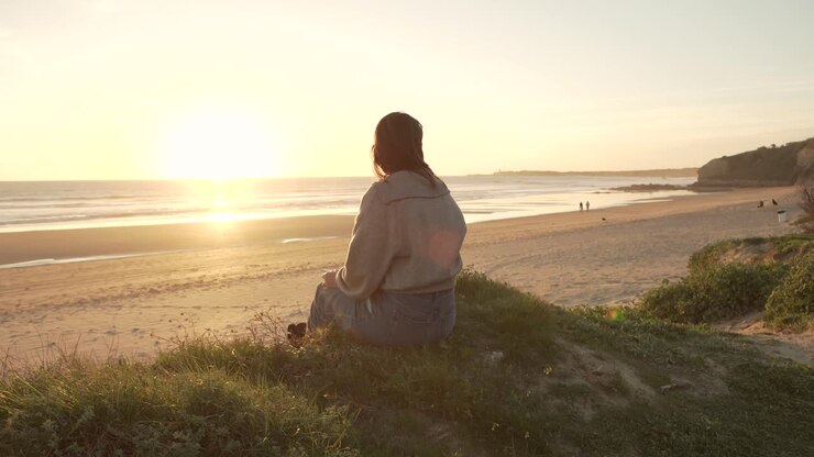 Mulher viajante sentada em uma colina com o céu do pôr do sol perto do mar