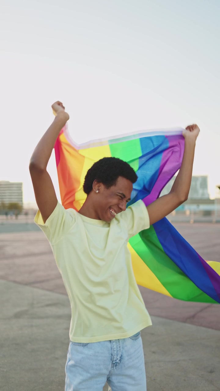 Happy Young Man Waving Rainbow Flag in Urban Setting at Sunset
