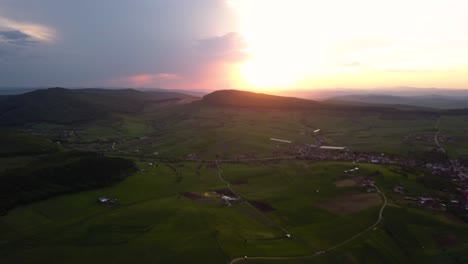 Toma-Aérea-Panorámica-De-Una-Hermosa-Puesta-De-Sol-Sobre-Campo-Abierto-Con-Verdes-Prados-Y-Campos,-Transilvania,-Rumania