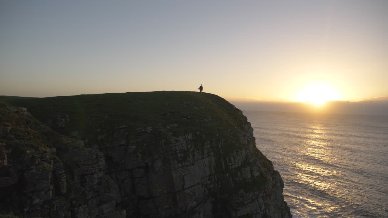 서핑 보드를 들고 바다를보고 일출 절벽의 가장자리에 남자