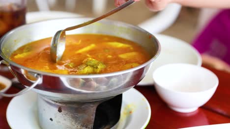 a person serves vibrant thai curry from a hot pot, highlighting traditional cuisine in a warm, inviting setting