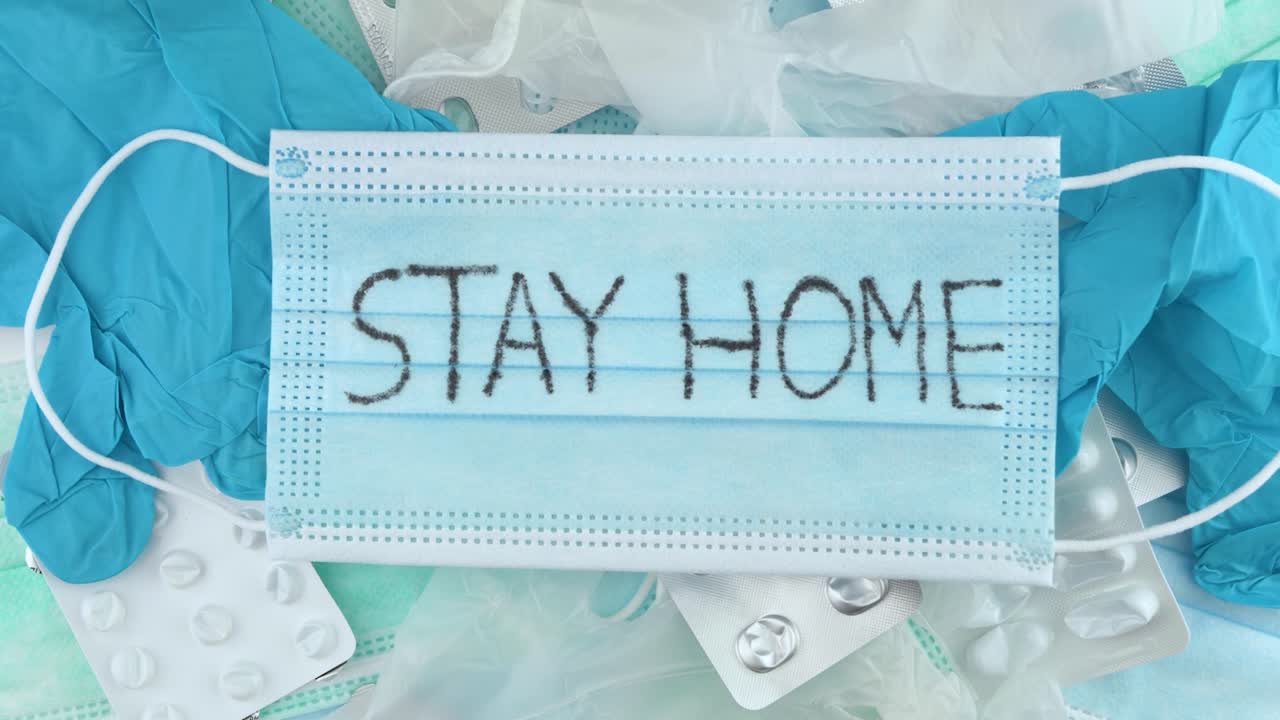 의료 폐기물 공급품 위의 안면 마스크에 쓰여진 '집에 있어' 경고 - 오버헤드 슬라이드 클로즈업 샷