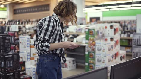 curious female customer choosing large tv-sets at electronics store, reading instruction for it. new screen generations. read closely tv specifications in the store