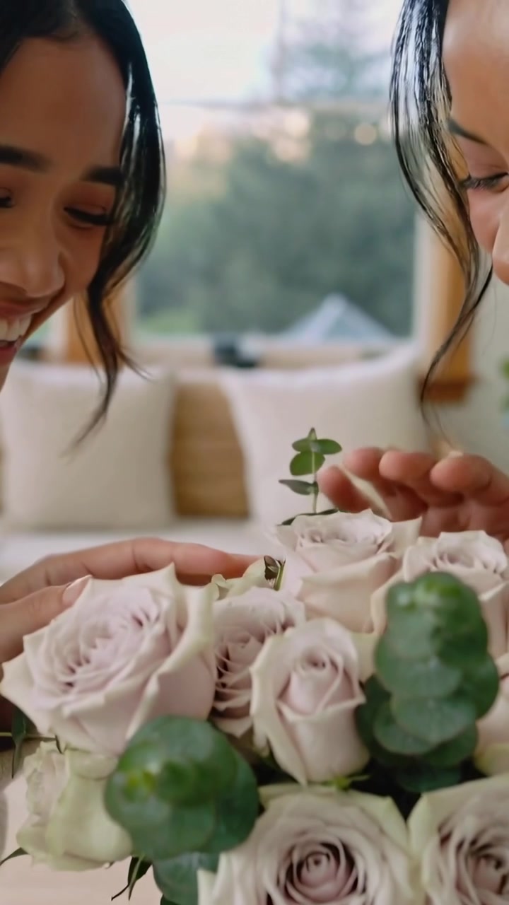 Vertical video: Handing bouquet two women in knit sweater exchanging stems at home, admiring roses