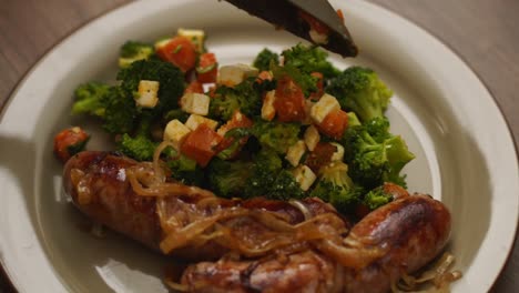 Anonymous-person-putting-salad-on-plate-with-sausages