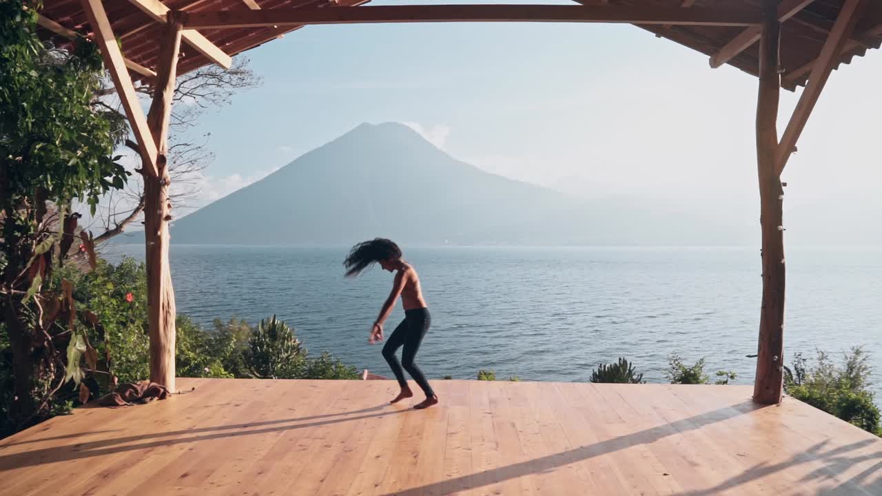 atractiva mujer delgada haciendo movimientos de baile modernos en el suelo de madera con un paisaje majestuoso detrás