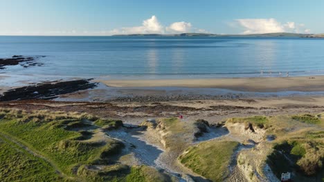 winter morning and an aerial over grassy dunes, sandy beach and calm ocean waters with blue sky and white clouds on a horizon