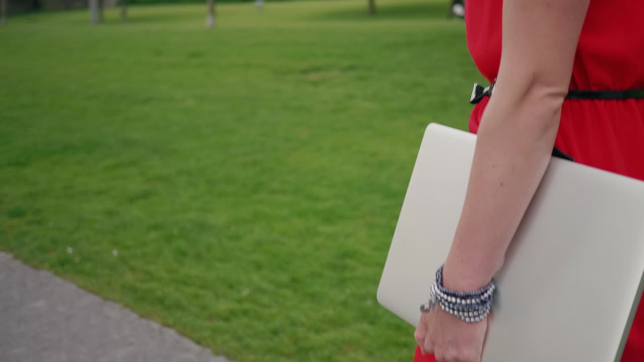 왼쪽에 복사 공간이 있는 노트북을 들고 공원의 포장 도로를 걷고 있는 여성의 세부 사진