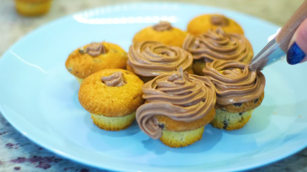 초콜릿 휘핑 크림으로 컵 케이크를 장식하는 여자의 손을 닫습니다