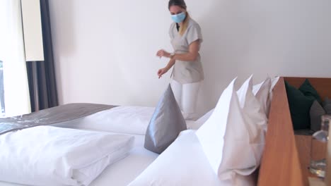 uma empregada doméstica com uma máscara facial prepara um travesseiro em um quarto de hotel