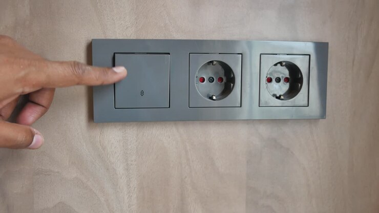 Person pointing at a wall switch and power outlet