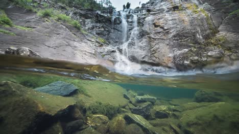 Vista-Espectacular:-Un-Río-Con-Bordes-Rocosos,-Aguas-Transparentes-Y-Una-Cascada-Lejana