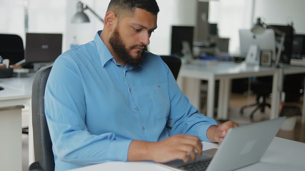 Confident bearded brunet working with laptop at modern office.