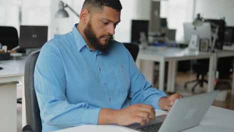 bruneta con barba segura trabajando con una computadora portátil en una oficina moderna.