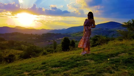 sunset over the mountains and a cloudy sky with a girl posing, spinning and jumping on a grassy hill