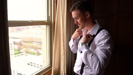 handsome groom getting ready by a window before the wedding