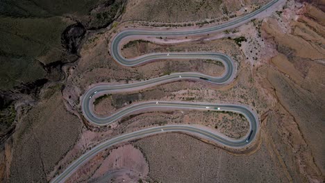 Static-top-down-drone-shot-showing-cars-and-trucks-driving-on-a-very-twisty-road-up-a-mountain-in-Jujuy,-Argentina