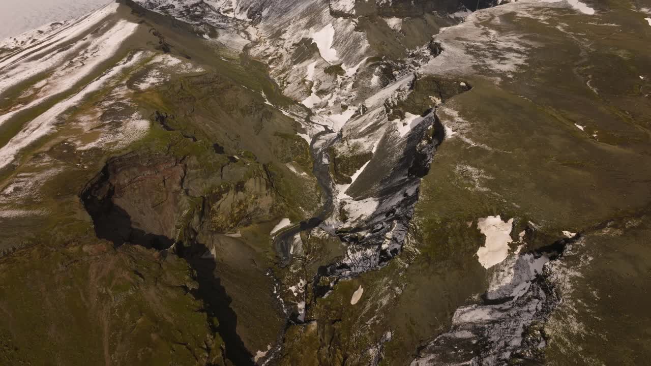 vista aérea del valle glacial de sólheimajökull, con montañas cubiertas de nieve, terreno escarpado y arroyos que fluyen