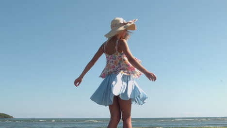 Attractive-blonde-with-straw-hat-spinning-on-the-beach