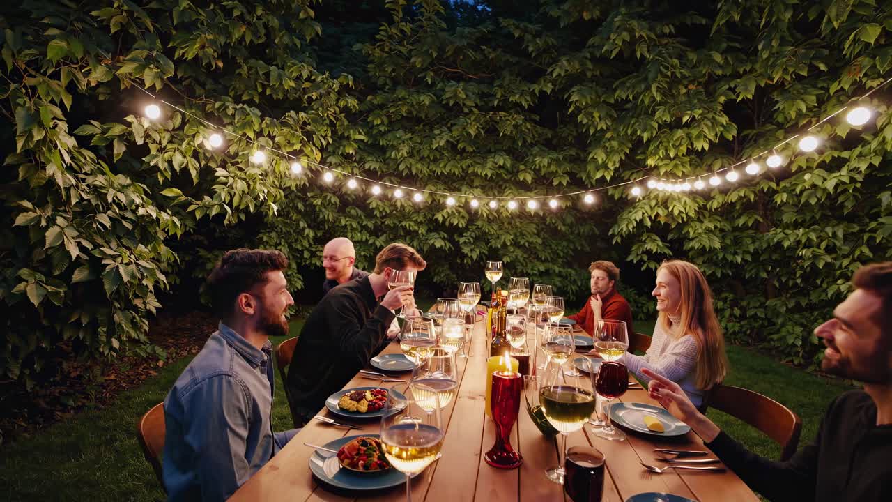 Aerial view of friends dining outdoors under string lights, creating a warm, inviting atmosphere