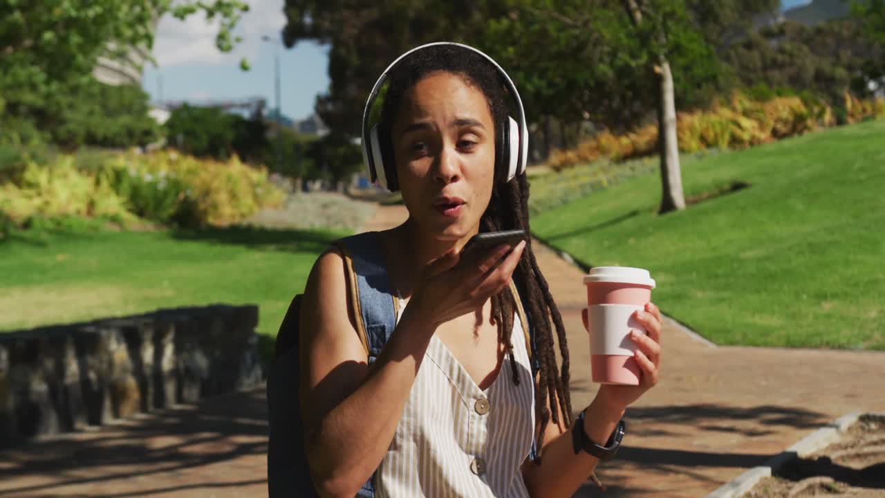 mujer afroamericana hablando en un teléfono inteligente sentada bebiendo café en el parque