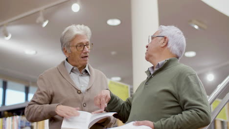 Senior-gray-haired-friends-discussing-book-in-public-library