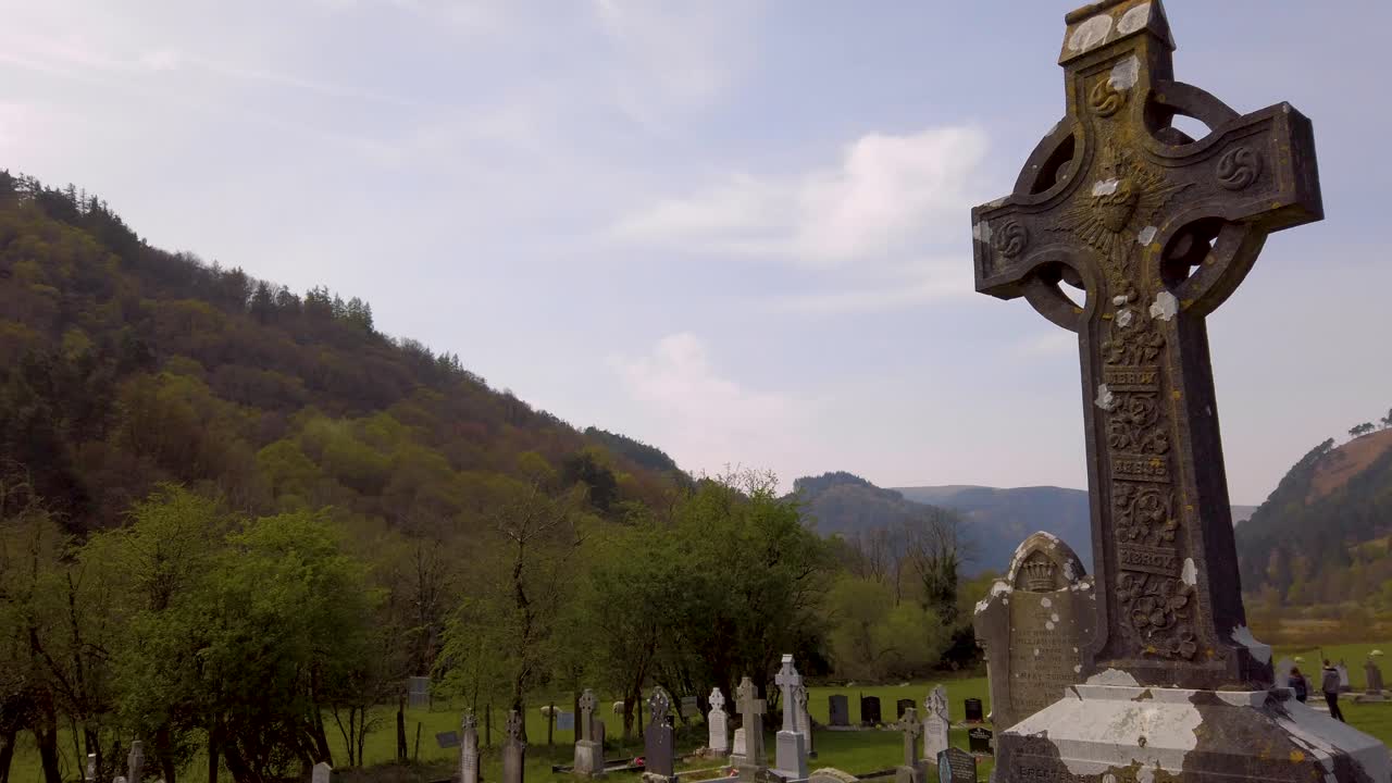 Tilt camera down on a large Irish Celtic rock cross in the middle of a cemetery.