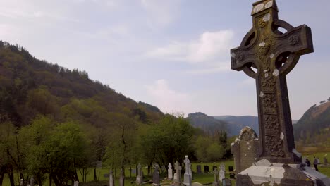 tilt camera down on a large irish celtic rock cross in the middle of a cemetery.