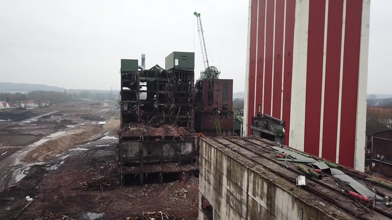 Un dron realiza un paso curvo alrededor de la torre de agua con una autopista con zona de camiones y un fondo urbano debajo.