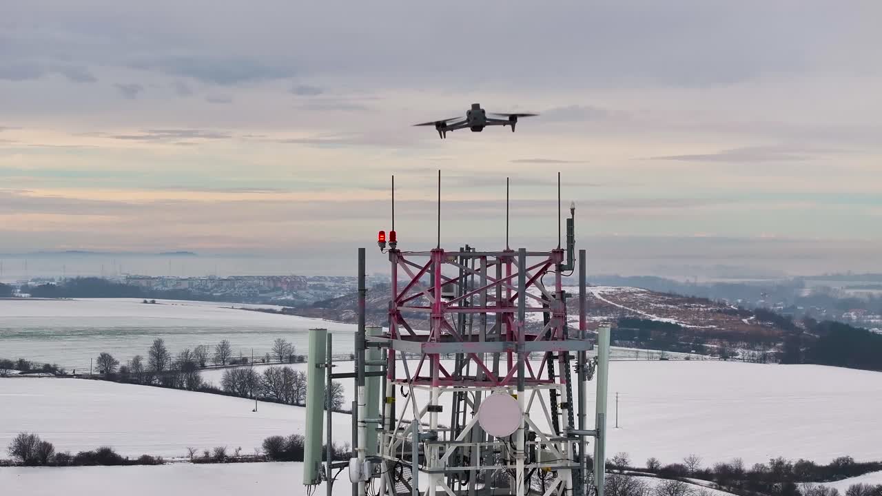 Drone flying near telecommunications tower in snowy winter landscape, Czechia