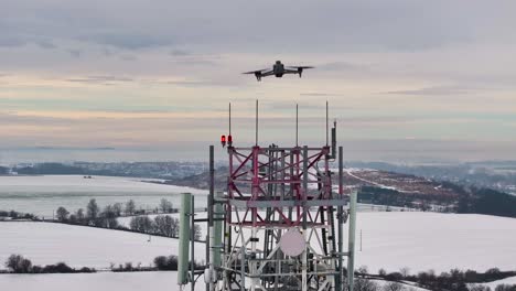 drone flying near telecommunications tower in snowy winter landscape, czechia