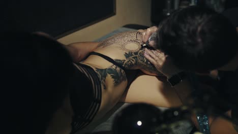 mujer obteniendo un tatuaje detallado negro y gris en la espalda y la cadera